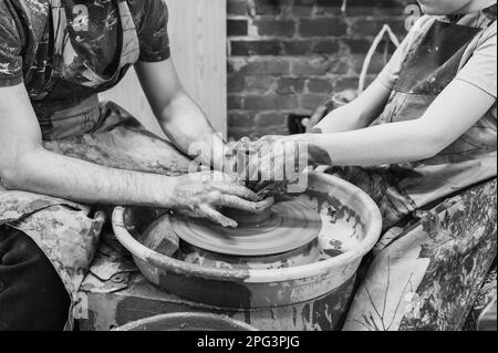 potter unterrichtet das Kind. Ein Handwerker sitzt auf einer Bank mit einem Töpferrad und macht einen Tontopf. Nationales Handwerk. Schwarzweißfoto. Stockfoto