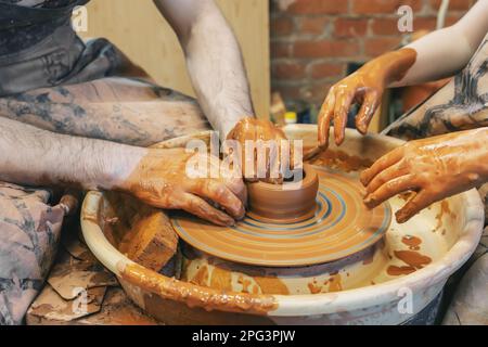 potter unterrichtet das Kind. Ein Handwerker sitzt auf einer Bank mit einem Töpferrad und macht einen Tontopf. Nationales Handwerk. Die Hände sind nah dran. Stockfoto