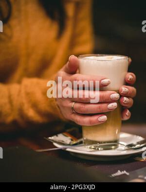 Eine Frau, die eine Tasse frisch zubereiteten, warmen Kaffee mit Schaum in der Hand hält Stockfoto