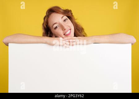 Entspannte rothaarige Frau, die sich auf eine leere Platte lehnt Stockfoto