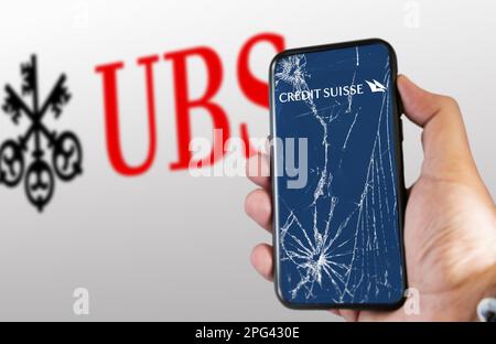 New York, USA, März 2023: Hand hält ein Telefon mit Credit Suisse Logo auf einem rissigen Bildschirm. UBS-Logo ist auf weißem Hintergrund verschwommen. UBS hat Credit Suis gekauft Stockfoto