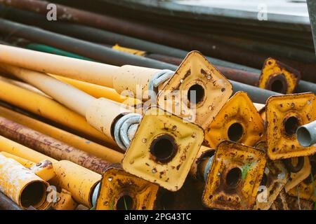 Alte Gerüstrohre werden im Freien in einem Stapel gelagert. Grundplatten für unterschiedliche gelbe Röhrchen. Teile des Gerüsts. Gerüstbasis Vintage Tapete. Stan Stockfoto