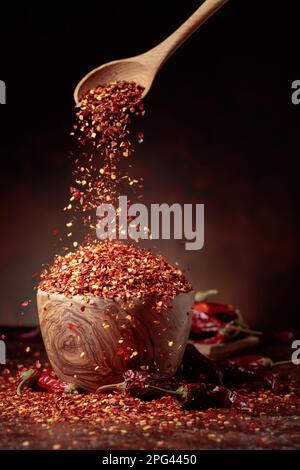 Chilischoten werden in eine Holzschale gegossen. Chilischoten und getrocknete Chilischoten auf braunem Hintergrund. Stockfoto