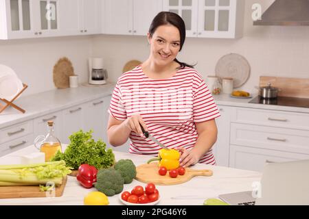 Schöne übergewichtige Frau, die eine gesunde Mahlzeit am Tisch in der Küche zubereitet Stockfoto