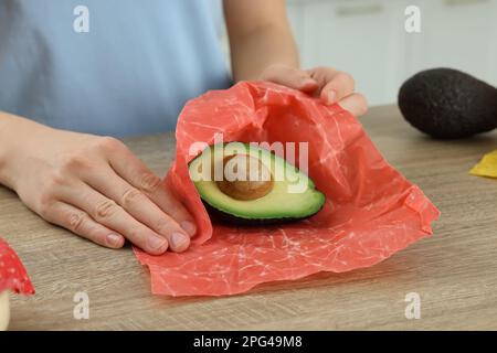 Eine Frau, die die Hälfte des Avocados in Bienenwachs verpackt hat, am Holztisch, Nahaufnahme Stockfoto