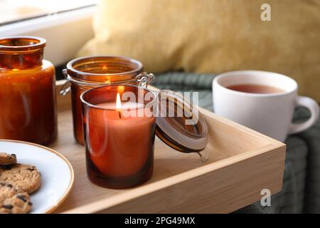 Tablett mit brennenden Kerzen und Keksen auf Fensterbank drinnen Stockfoto