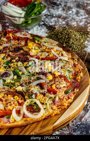 Eine frisch zubereitete Pizza auf einem Holzbrett neben anderen verschiedenen Speisen Stockfoto
