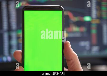 Schwarzes Telefon mit leerem Mockup-Bildschirm auf steigendem Aktiendiagramm. Nahaufnahme-Hand zeigt isoliertes grünes Display des Smartphones. Online-Banking, Nutzung von Fonds-Apps. Fina Stockfoto