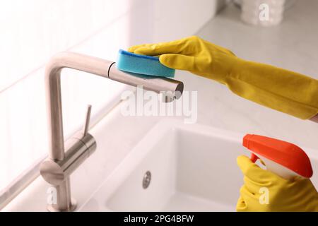 Frau, die den Wasserhahn mit Schwamm und Reinigungsmittel in der Küche reinigt, Nahaufnahme Stockfoto