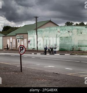 Kleine Karoo-Städte haben eine hohe Arbeitslosenquote. Hier, in der Hauptstraße durch Hofmeyr, „hängen“ Einheimische in einer Gruppe herum. Viele ältere Unternehmen A Stockfoto