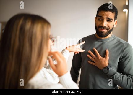 Verheiratetes internationales Millennials-Paar streitet sich, Frau zeigt mit dem Finger auf Ehemann im Wohnzimmer Stockfoto