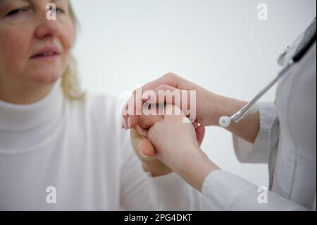Freundliche männliche Arzthandschuhe halten weibliche Patienten zur Ermutigung und Mitgefühl an der Hand. Partnerschaft, Vertrauen und medizinethisches Konzept. nachrichtenreduzierung und Unterstützung. Patientenjubel und -Unterstützung Stockfoto