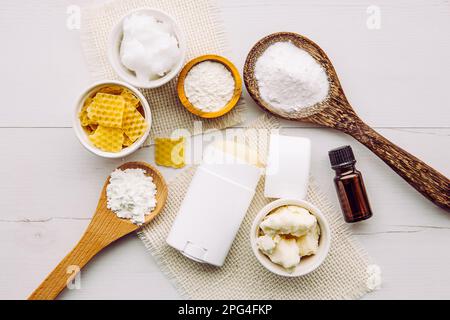 Konzept für die Herstellung von selbstgemachtem Deodorant mit allen natürlichen Inhaltsstoffen. Weißer Holzhintergrund. Zutaten: Pfeilwurzpulver, Backpulver, Bienenwachs. Stockfoto