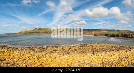 Orangefarbene Tonfelsen im Vordergrund mit Blick auf Kimmeridge Bay und Jurassic Klippen und Parkplatz an einem sonnigen Tag mit leichten Wolken Stockfoto