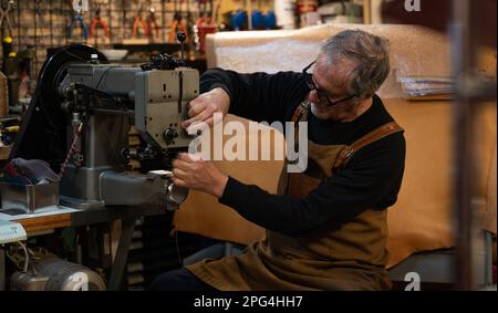 Ein erwachsener Handwerker, der in einer Nähmaschine Faden hinzufügt, um in seiner Werkstatt in der Innenstadt von rom, italien, mit dem Nähen von Teilen eines Lederstuhls zu beginnen Stockfoto