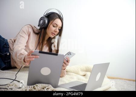 Eine wunderschöne junge indische Asiatin hört Musik auf ihren kabellosen Kopfhörern, während sie tagsüber in einem angesagten Café an ihrem Laptop arbeitet. . Hochwertiges Foto Stockfoto