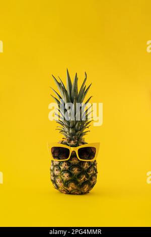 Frische Ananas mit Sonnenbrille auf gelbem Hintergrund. Minimales Sommerfurit-Konzept. Stockfoto