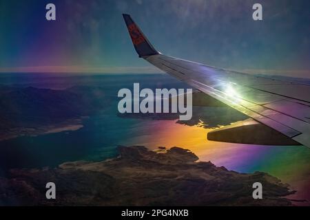 Sun Countries Airlines Flugzeug Flug hoch über die Berge und Hügel von Colorado mit dem Sonnenlicht, das vom Flugzeug und vom Wasser reflektiert wird. Stockfoto