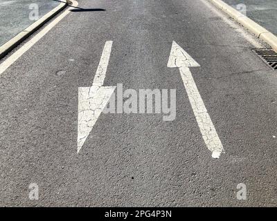 Weiße Pfeile in die entgegengesetzte Richtung auf einer asphaltierten Stadtstraße. Konzept der einzuschlagenden Richtung. Stockfoto