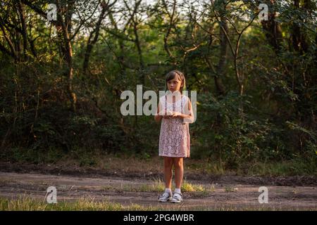 Ein Mädchen mit grünem Haar hat sich im Wald verlaufen. Das Kind steht verängstigt auf dem Weg im Lichtstrahl zwischen den Bäumen, nervös am Fangen Stockfoto