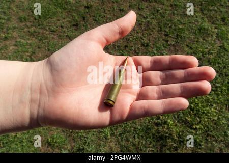 Gewehrkartusche in der Hand auf grünem Gras. Nahaufnahme Stockfoto