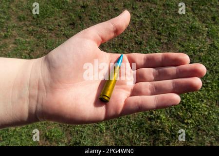 Gelbblaues Gewehrkartuschen in der Hand vor grünem Gras (nationale Symbole der Ukraine). Das Konzept der militärischen Unterstützung für die Ukraine Stockfoto