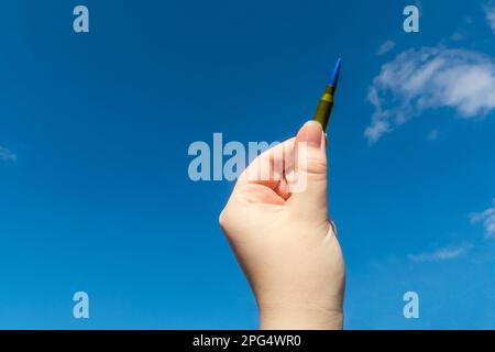 Gelbblaue Gewehrkassette in der Hand vor dem blauen Himmel (nationale Symbole der Ukraine). Das Konzept der militärischen Unterstützung für die Ukraine Stockfoto