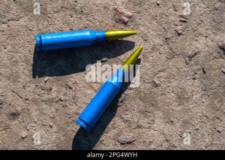 Zwei gelb-blaue Gewehrpatronen (das nationale Symbol der Ukraine) liegen auf einer Betonoberfläche (Nahaufnahme). Das Konzept der militärischen Unterstützung für die Ukraine Stockfoto