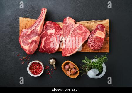 Rohe Prime Steaks. Auswahl an frischen schwarzen angus Prime Steaks T-Bone, New York, Ribeye, Striploin, Tomahawk Schneidebrett auf schwarzem oder dunklem Hintergrund Stockfoto