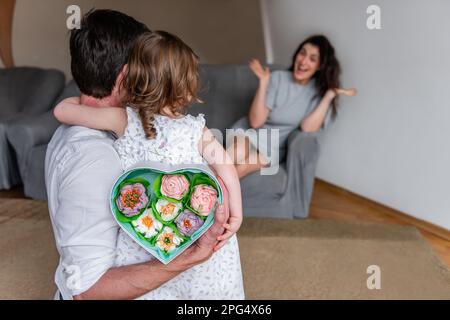 Kleine Tochter und Vater halten ein Geschenk für Mutter hinter dem Rücken, herzförmige Box mit hausgemachten Marshmallow-Blumen. Überraschung für Frauen am Muttertag fr Stockfoto