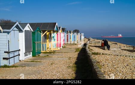 Row of Beach Huts am Calshot Beach mit Einem Containerschiff im Hintergrund, das in Solent, Calshot UK einläuft Stockfoto