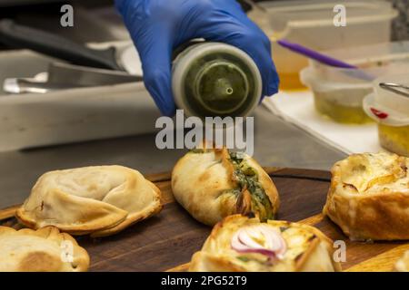 Ein Koch, der Soße mit einer Flasche auf gebackenen Empanadas gießt Stockfoto