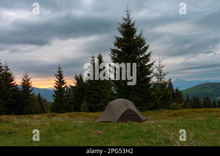 Grünes, leichtes, freistehendes Zelt für 2 Personen in drei Jahreszeiten auf Bergkohle im Gras am Morgen. Im Hintergrund: Mala-Fatra-Gebirge, Slowakei. Stockfoto