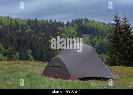 Grünes, leichtes, freistehendes Zelt für 2 Personen in drei Jahreszeiten auf Bergkohle im Gras am Morgen. Im Hintergrund: Mala-Fatra-Gebirge, Slowakei. Stockfoto