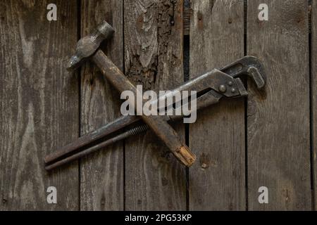 Alter rostiger Gasschlüssel und Hammer liegen auf einem Holztisch in Nahaufnahme Stockfoto