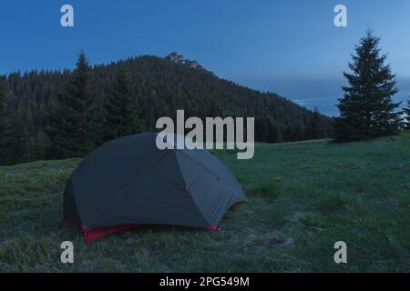 Grünes, leichtes, freistehendes Dreijahreszelt für 2 Personen auf Bergkohle im Gras am Abend. Zum Hintergrund: Velky Rozsutec. Die Mala Fatra Berge Stockfoto