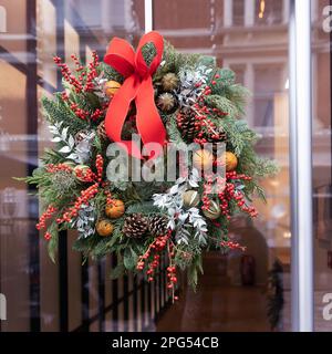 Weihnachtskranz aus Tannenzweigen mit Dekorationen, die an der Wand des Hauses hängen Stockfoto