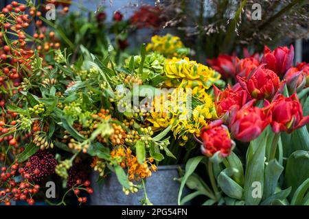 Skimmia japonica, Holly, Hypericum rote Tulpen, gelbe Rosen, Feldkräuter und trockener Spargel werden zu weihnachten zum Verkauf angeboten. Bouq Stockfoto