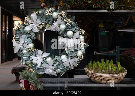 Ein Weihnachtskranz aus künstlichen Eukalyptuszweigen mit Schleifen und weißen Glaskugeln schmückt den Innenhof. Auf dem Tisch liegt ein Korb mit hya Stockfoto