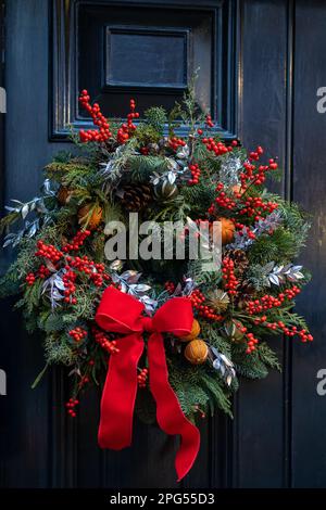 Weihnachtskranz aus Tannenzweigen mit Dekorationen, die an der Wand des Hauses hängen Stockfoto