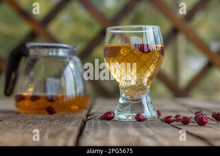 Roter Tee in einer durchsichtigen Tasse auf einem Holztisch, Rosehip-Tee, Teetrinken in einem rustikalen Pavillon Stockfoto