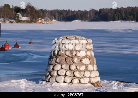 Helsinki / Finnland - 9. MÄRZ 2023, Ein von Menschenhand geschaffener Felsenhaufen an einem gefrorenen See an einem sonnigen Wintertag Stockfoto