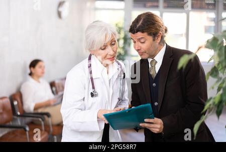 Aufmerksame leitende Ärztin verschreibt Tests an Patienten der Klinik, um den Gesundheitszustand zu überprüfen Stockfoto