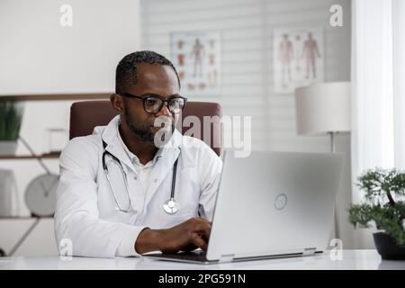 Ein afroamerikanischer Arzt begrüßt die Online-Patientenberatung auf dem Laptop. Ein Büro, das telemedizinische Dienste erbringt. Online-Medizin und Stockfoto