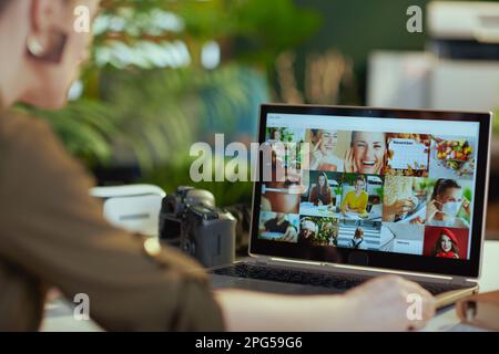 Fotografin mit Laptop und Fotokamera, die Fotos in einem modernen Büro ansieht. Stockfoto