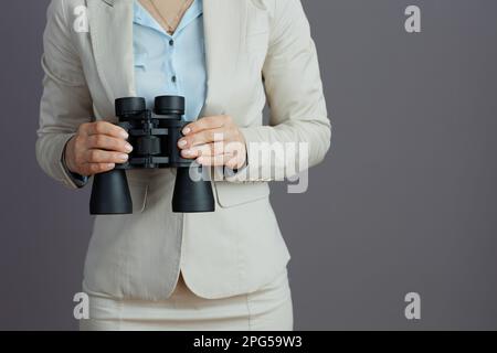 Nahaufnahme einer Geschäftsfrau mittleren Alters in einem leichten Business-Anzug mit Fernglas isoliert auf grauem Hintergrund. Stockfoto