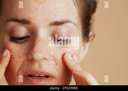 Nahaufnahme einer Frau mittleren Alters mit Gesichtspeeling auf beigefarbenem Hintergrund. Stockfoto