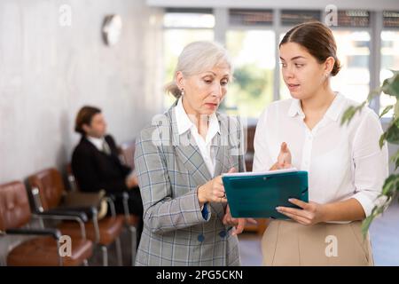 Ältere und junge Frau, die mit Dokumenten in die Akte schaut Stockfoto