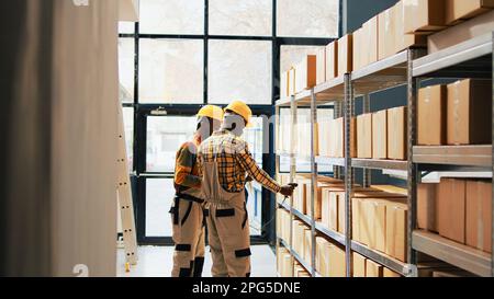 Team von Mitarbeitern, die mit Scanner und Warenliste an der Logistik arbeiten und den Vertrieb mit Warenbestand planen. Zwei Männer scannen Produkte im Einzelhandel auf Regalen im Depot. Handgeführte Aufnahme. Stockfoto