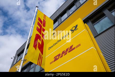 Aschheim, Deutschland. 20. März 2023. Ein Schild und eine Flagge mit dem DHL-Logo stehen am DHL-Paketcenter. Durch die Anbindung an das bestehende Paketzentrum entsteht der größte Paketabfertigungsstandort von Deutsche Post DHL in Deutschland. Kredit: Sven Hoppe/dpa/Alamy Live News Stockfoto